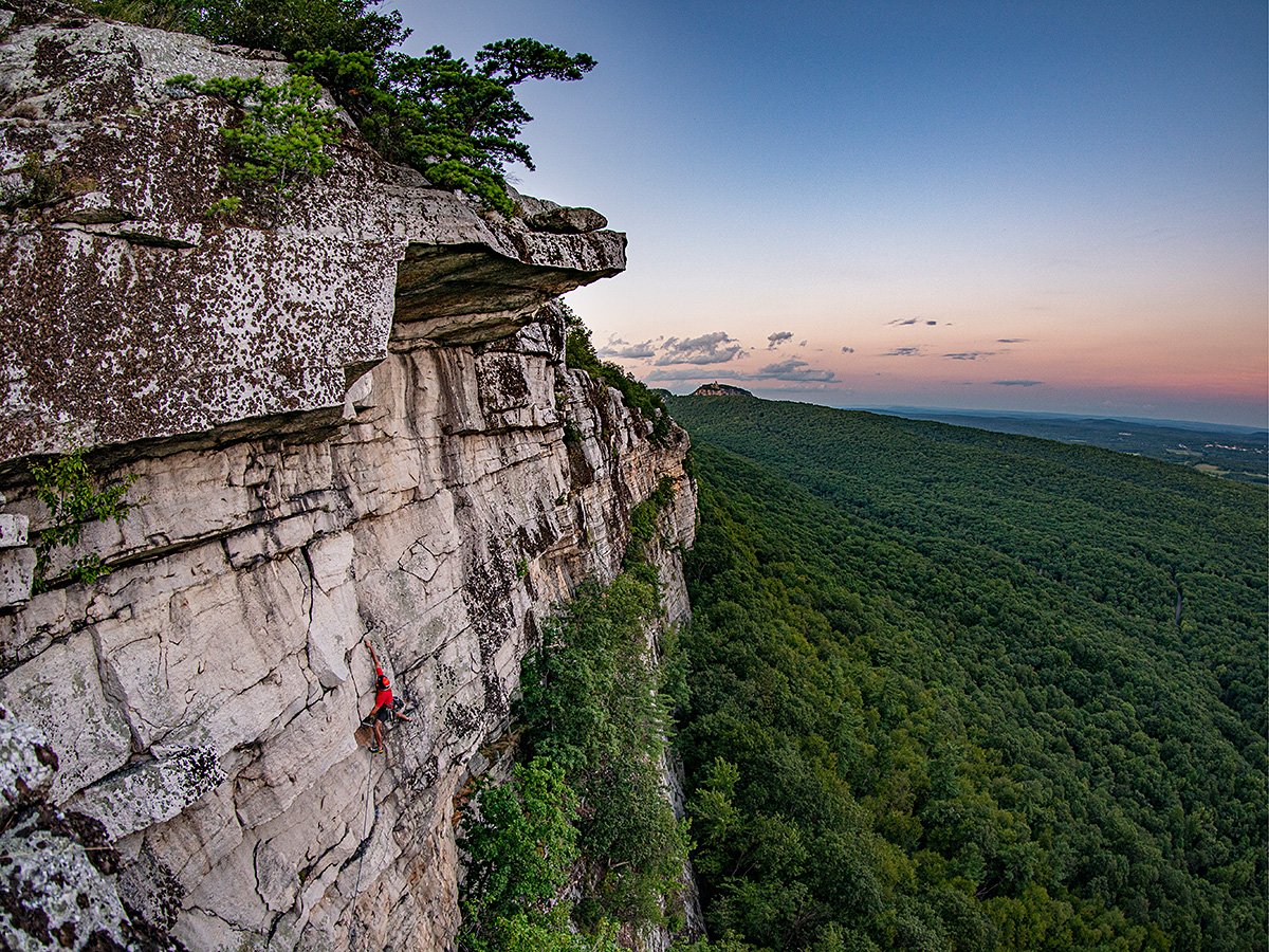 Climber on a mountain with a lush green set of forest in the background